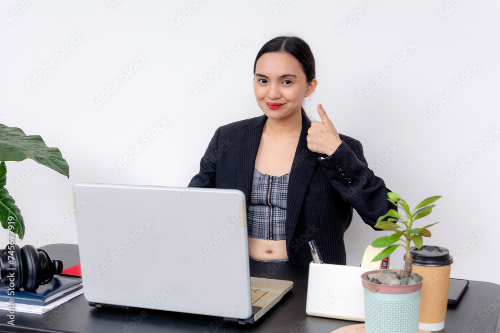 A young Asian businesswoman in a blazer gives thumbs up at her office, signaling approval and support for new policies. In casual wear covered with a blazer. A young Asian businesswoman in a blazer gives thumbs up at her office, signaling approval and support for new policies. In casual wear covered with a blazer.