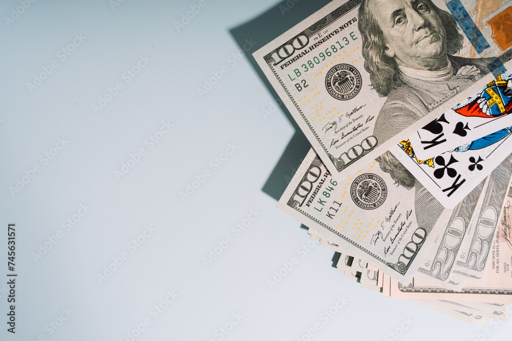 Dollar bills of different denominations with playing cards on a light background
