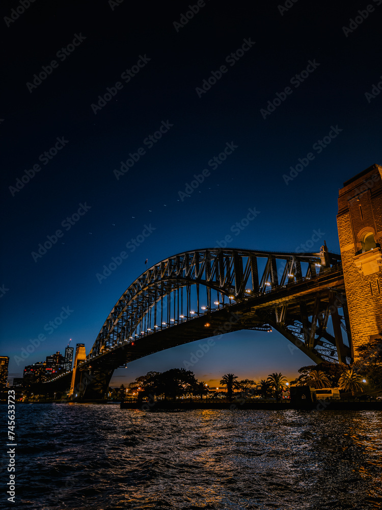 Obraz premium Sydney by night and at sunset is a beautiful sight to behold. The city skyline, complete with the iconic Harbour Bridge, is a picture-perfect view of Australia.