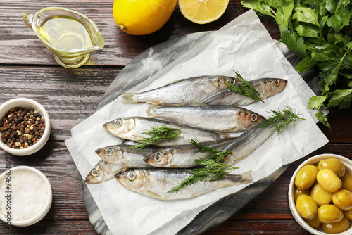 Fresh raw sprats, dill and other products on wooden table, flat lay