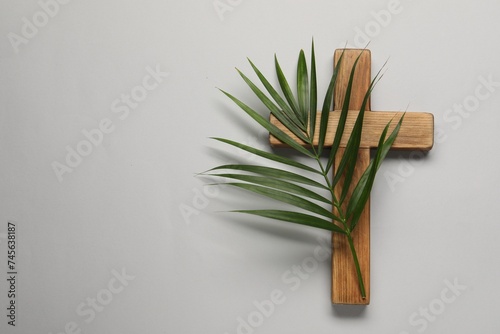 Wooden cross and palm leaf on light grey background  top view with space for text. Easter attributes