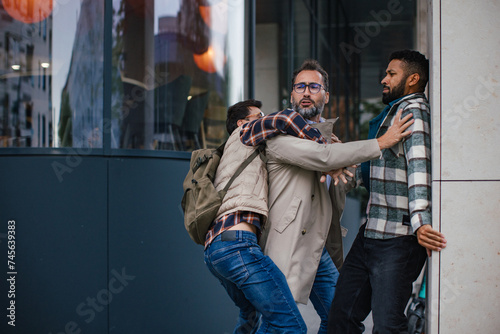 Angry man is aggressive, have conflict with young man, holding him by shirt, screaming, threatening him. Friend helping to end fight. photo