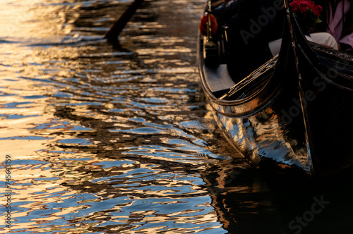 Symbolbild für Wenig Reisen, Morgensonne spiegelt sich im Kanal und reflektiert auf dem glatten schwarzen Rumpf einer Gondel.