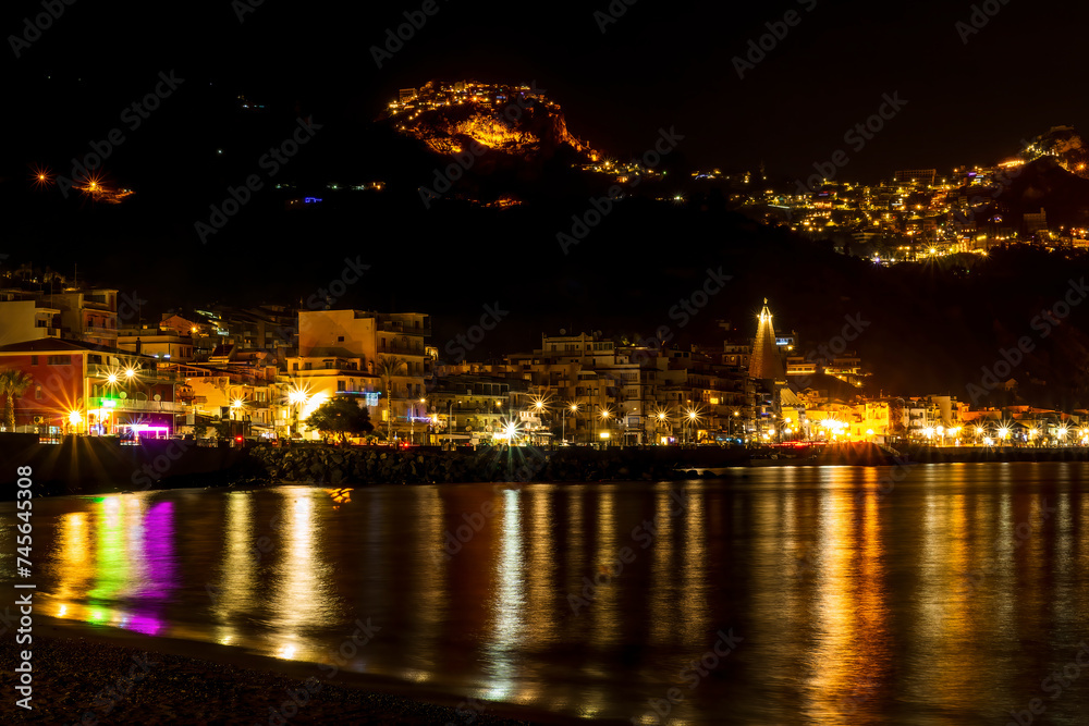 night town coast with flashlights from embarkment and reflection in sea gulf water with golden urbal lights on background of landscape