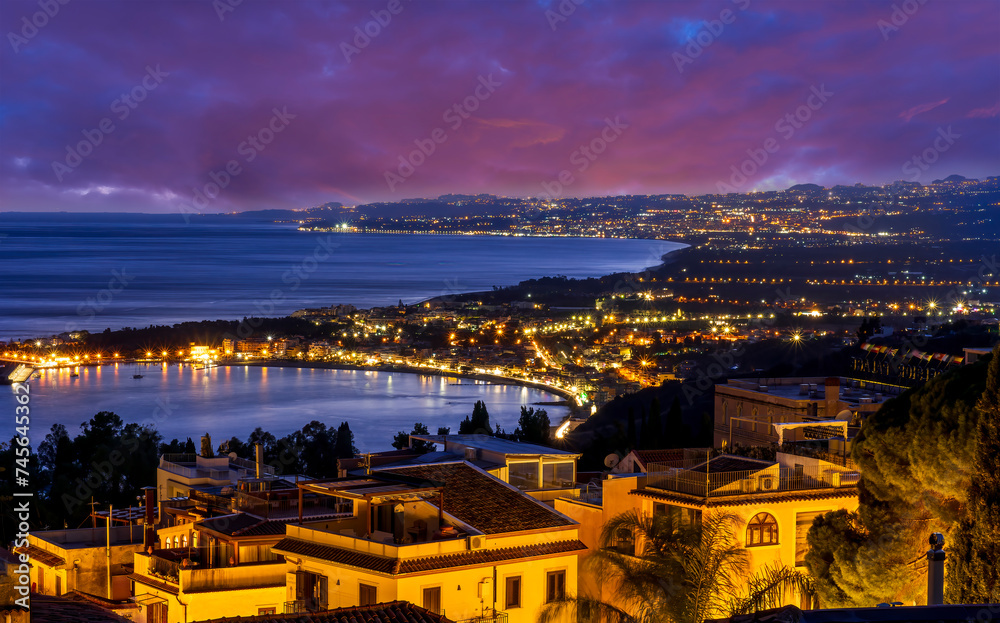 beautiful night european town in golden lights with sea shore and nice sunset sky on background