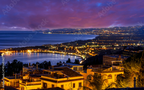 beautiful night european town in golden lights with sea shore and nice sunset sky on background