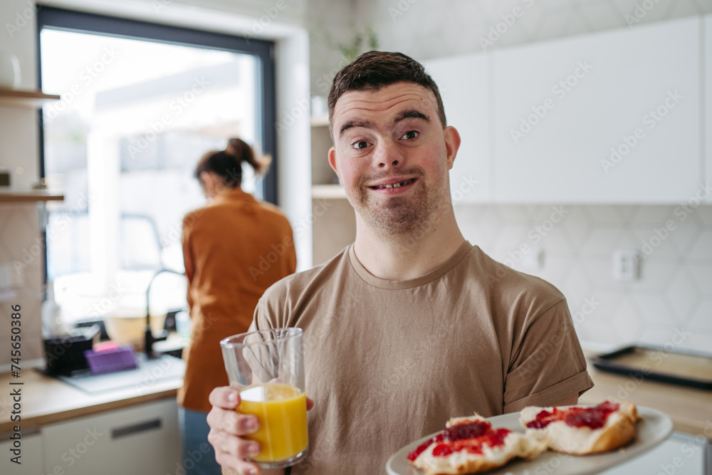 Young man with Down syndrome holding breakfast and glass of juice. Morning routine for man with Down syndrome. Young man with Down syndrome holding breakfast and glass of juice. Morning routine for man with Down syndrome.