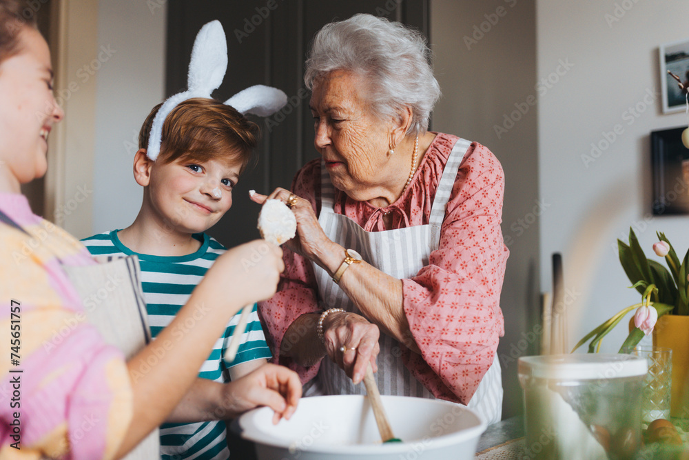 Grandmother with grandchildren baking cakes and sweets for easter, having fun. Boy with cake batter on nose. Passing down family recipes, custom and stories.