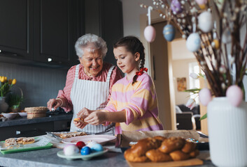 Grandmother with grandaughter preparing traditional easter meals, baking cakes and sweets. Passing down family recipes, custom and stories.