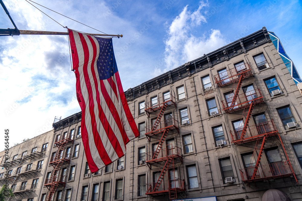 Large American flag flying in front of a red brick building with a blue sky in the background