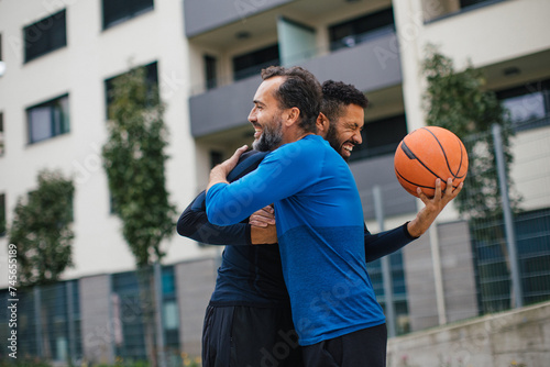 Best friends playing sport outdoors, having fun, hugging after game. Playing basketball at a local court, enjoying exercise together. Concept of male friendship, bromance. © Halfpoint
