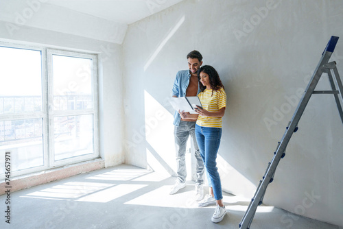 Couple using tablet PC and analyzing blueprint for renovation at new home photo