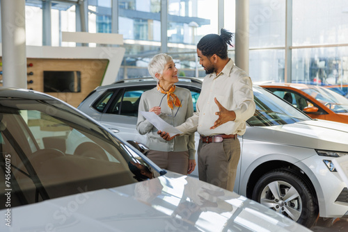 Salesperson discussing with smiling customer in car showroom photo