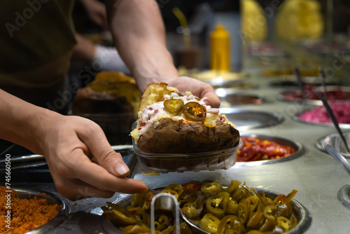 Turkish street food Kumpir. Male cook adds different fillings to the Kumpir. Delicious baked potatoes with a variety of mixed fillings