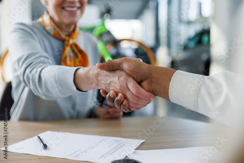 Smiling woman shaking hands with car salesperson at desk