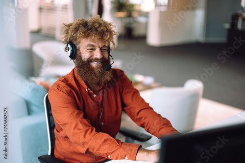 Happy businessman wearing headset and working on computer in office photo