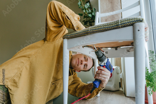 Smiling man using drill on chair at home photo