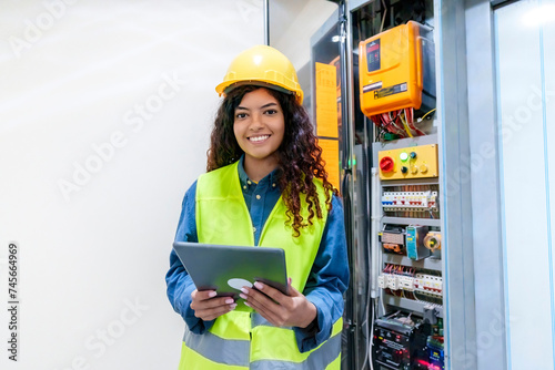 Smiling engineer holding tablet PC by electric fuse box photo