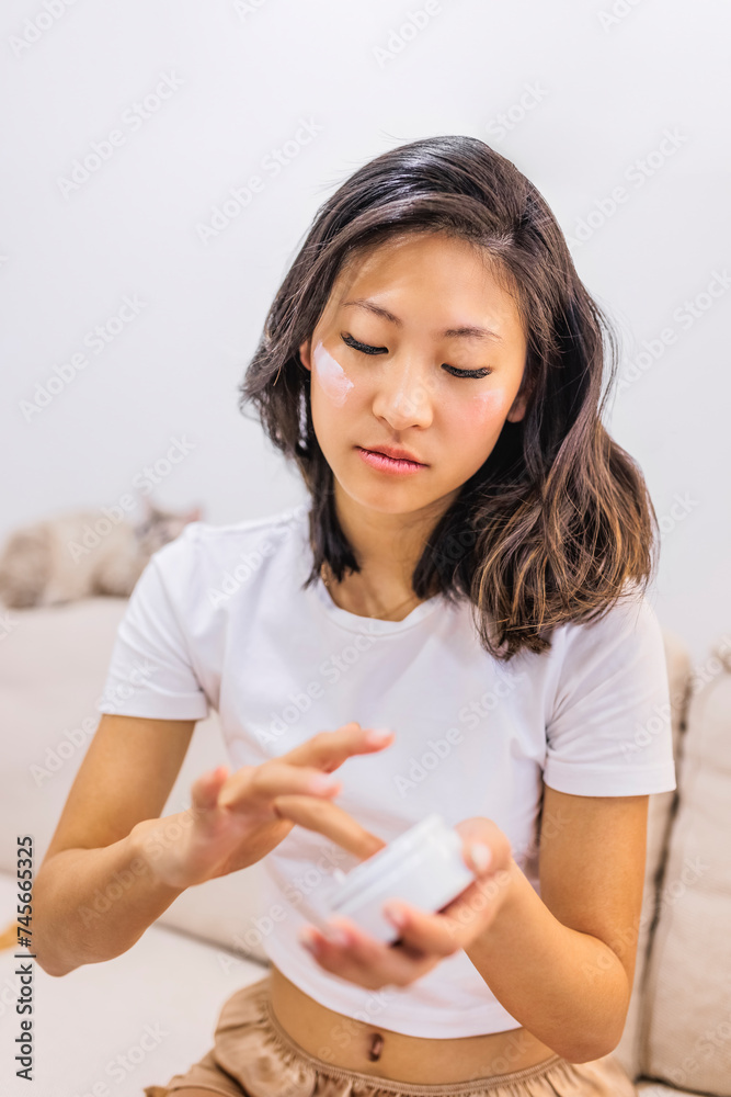 Young woman applying moisturizer on face at home Young woman applying moisturizer on face at home