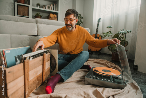 Man listening to vinyl records sitting with box full of disks at home photo