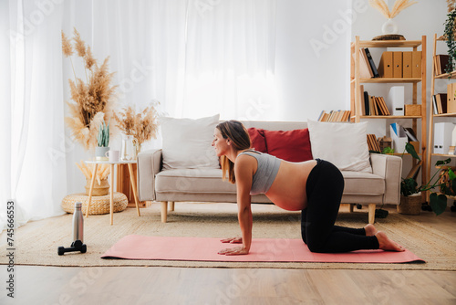 Pregnant woman practicing cow pose on yoga mat at home photo