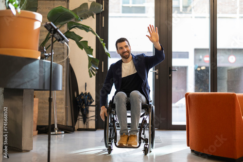 Smiling businessman in wheelchair with disability waving at workplace
