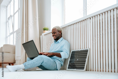 Smiling freelancer sitting near solar panel and using laptop at home photo