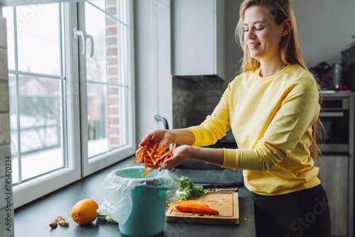 Smiling woman putting carrot leftovers in garbage can at home photo