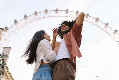 Happy couple standing in front of Ferris wheel under sky in London