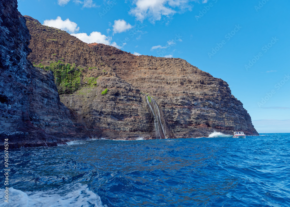 View from a tourist boat of a stunning cliff in the Pacific ocean and a small boat at Napali Coast, Island of Kauai, Hawaii