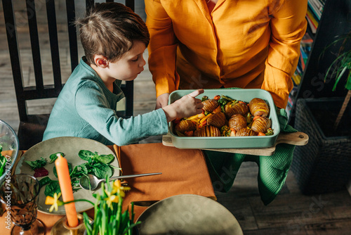 Hungry boy picking up fried potatoes from casserole dish held by grandmother at Easter dinner photo