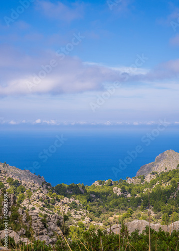 Amazing landscapes of Mallorca. The mountains are covered with greenery, the sea is blue and transparent. Sunny day, clouds over a rocky ridge. Mallorca, Spain, Balearic Islands