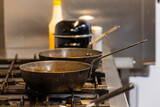 This image provides a glimpse into a professional kitchen, focusing on two empty woks positioned on a gas range. The kitchen equipment, including the woks and the gas range, appear seasoned from