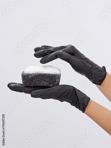 A woman's hand in even gloves holds a black dishwashing sponge