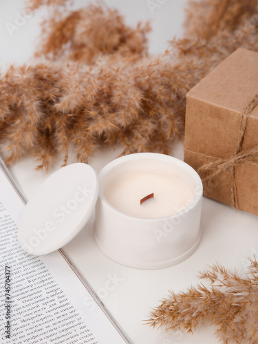 candle with a lid on a white table surrounded by craft boxes and reed branches