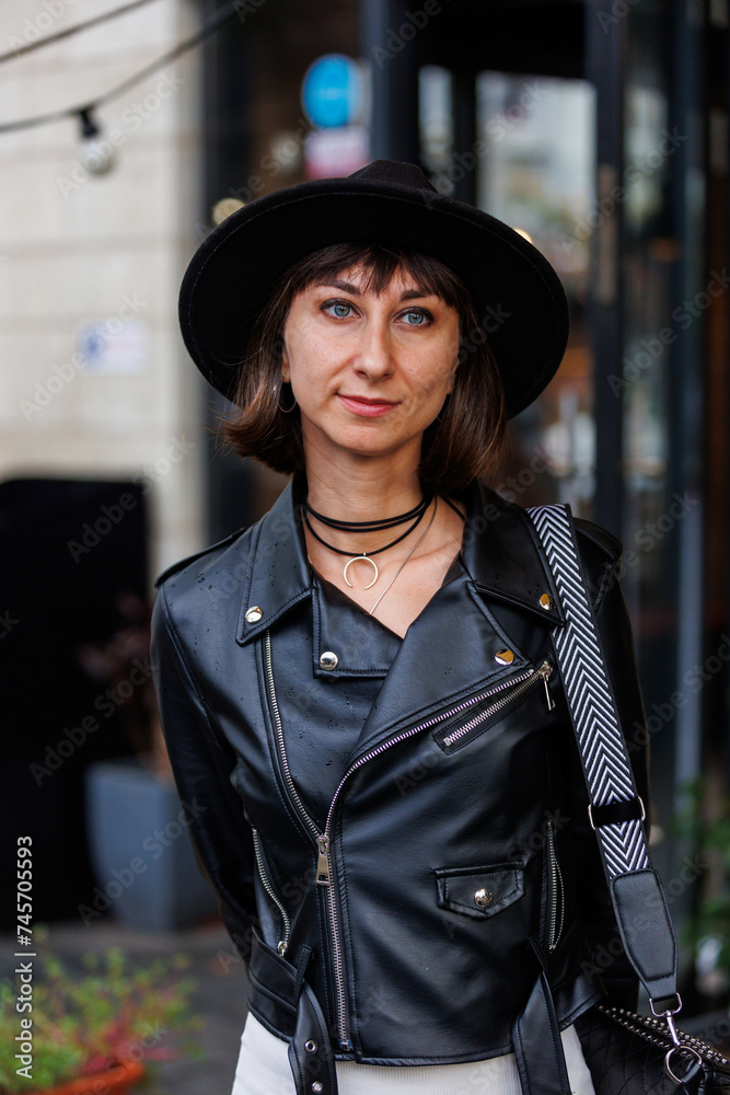 Fashionable woman in a hat, black stylish leather jacket and dress portrait of a girl on the street.
