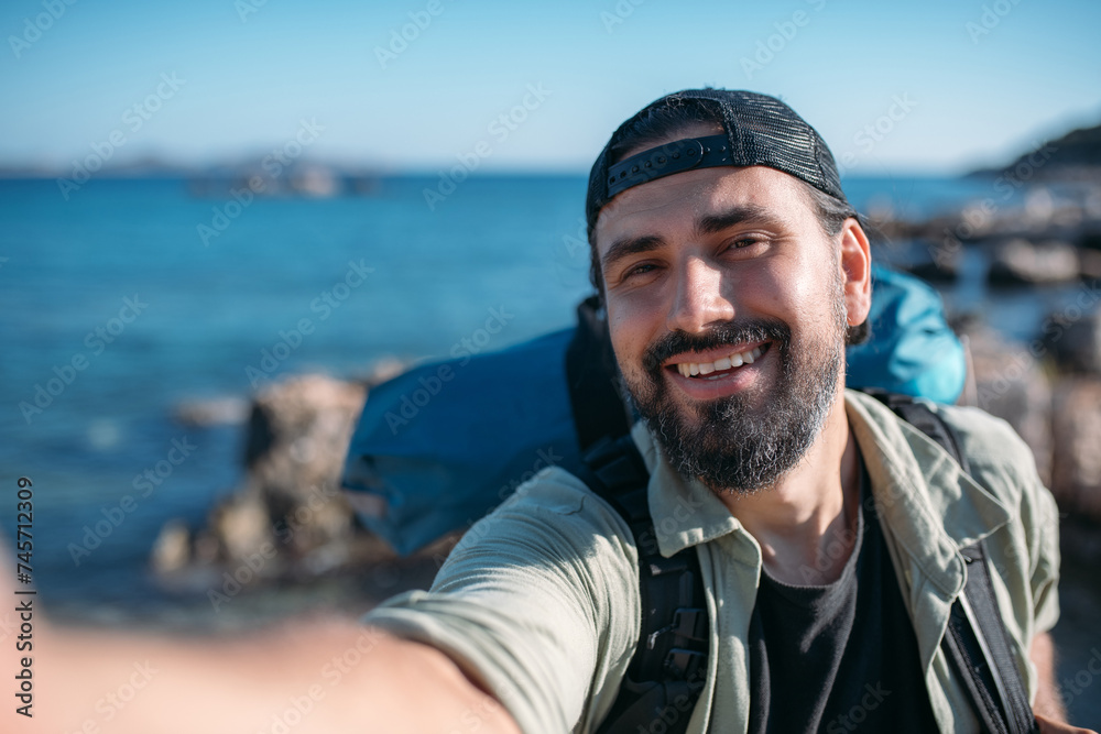A male tourist with a large backpack and hiking gear takes a selfie. A male tourist with a large backpack and hiking gear takes a selfie.