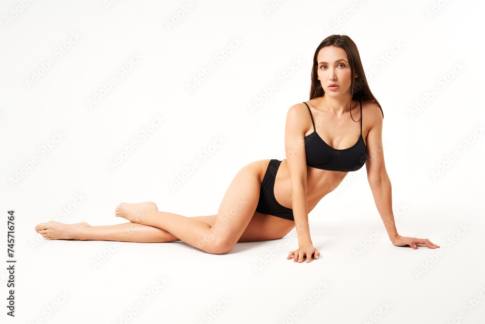 Young beautiful woman with perfect body in black underwear sitting on floor posing on studio