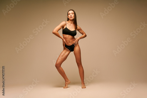 Pretty sporty woman in black underwear posing on beige studio background