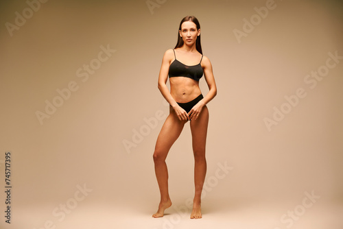 Pretty sporty woman in black underwear posing on beige studio background © GVS