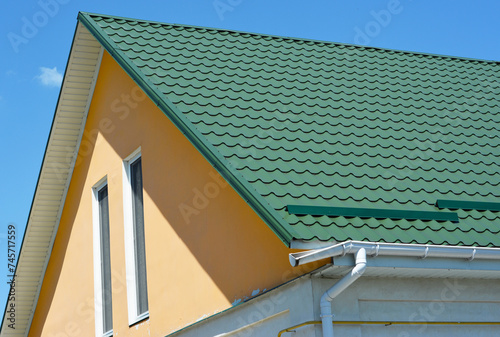 Close up on house rooftop facade with metal roof and broken plastic rain gutter pipeline.