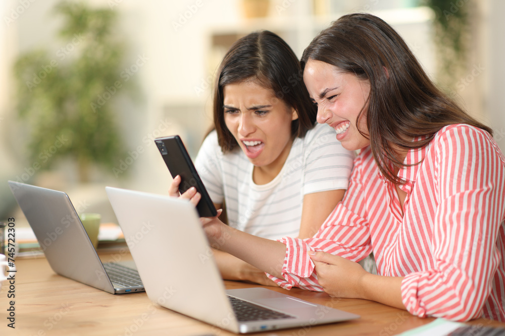 Two disgusted women checking nasty content on phone Two disgusted women checking nasty content on phone