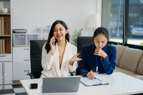 Female discussing new project with Female colleague. Young women talking with young Asian man in office.