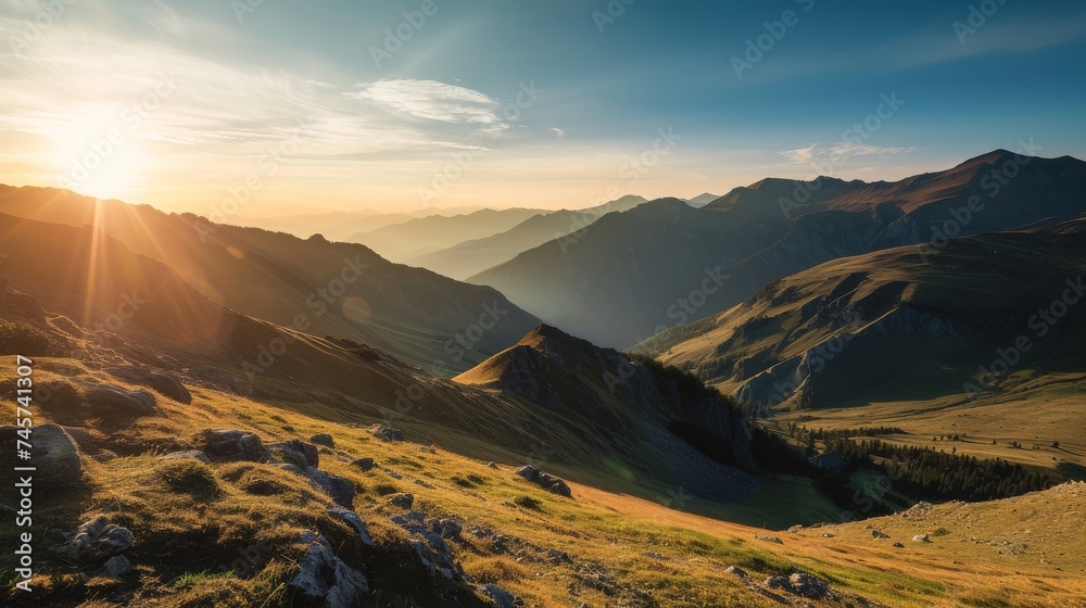 A serene, high definition landscape photo of a mountain range at sunrise. The image should highlight the soft, warm glow of the sun casting long shadows across the rugged terrain.
