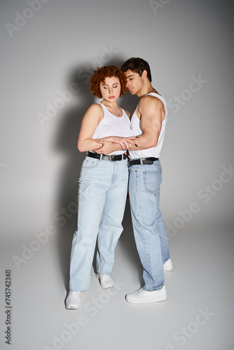 beautiful boyfriend and girlfriend in casual attire hugging lovingly on gray backdrop, sexy couple