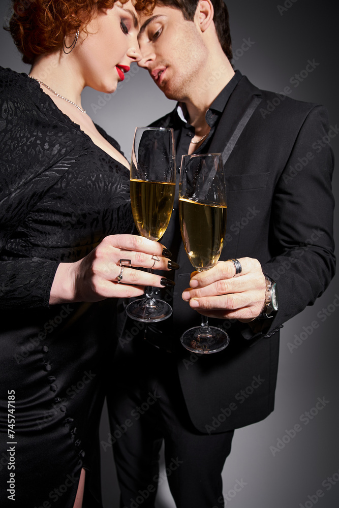 alluring woman in black dress hugging her handsome boyfriend on gray backdrop, champagne in hands alluring woman in black dress hugging her handsome boyfriend on gray backdrop, champagne in hands