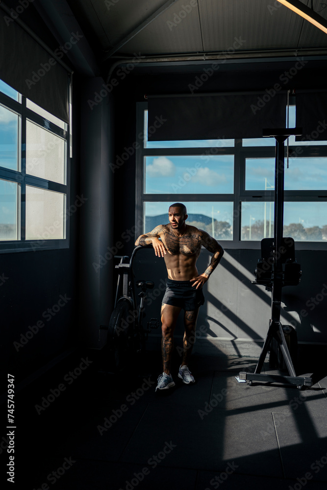 Chico joven tatuado y musculoso posando en gimnasio sin camiseta y con ropa moderna Chico joven tatuado y musculoso posando en gimnasio sin camiseta y con ropa moderna