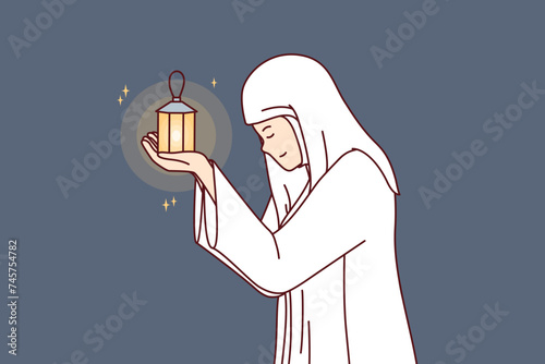 Muslim woman prays in holy month of ramadan and holds lantern for islamic ritual in hands, dressed in white robe. Muslim girl demonstrates repentance and humility before allah almighty