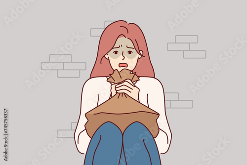 Woman suffering from panic attack holds paper bag for hyperventilation and restoration of normal psychological state. Girl sitting on floor near brick wall and experiencing stress due to panic attack