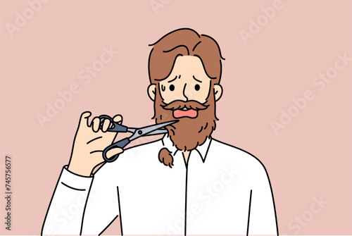 Man cuts off own beard with scissors because of appearance requirements at new job. Adult depressed guy is stressed due to need to get rid of beard or lack of money to go to barbershop. 